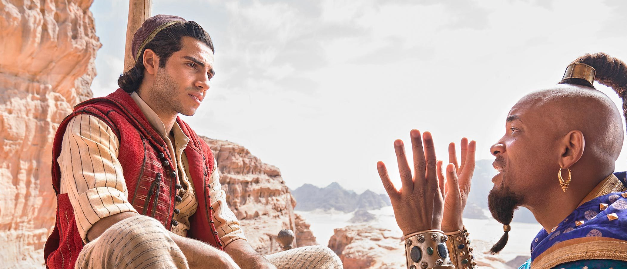 Two characters from the film Aladdin sitting together talking on a rocky desert ledge
