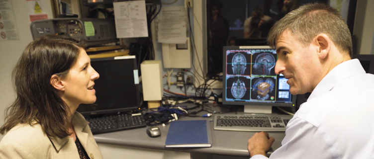 Two researchers discussing brain scan images displayed on a computer monitor in a lab